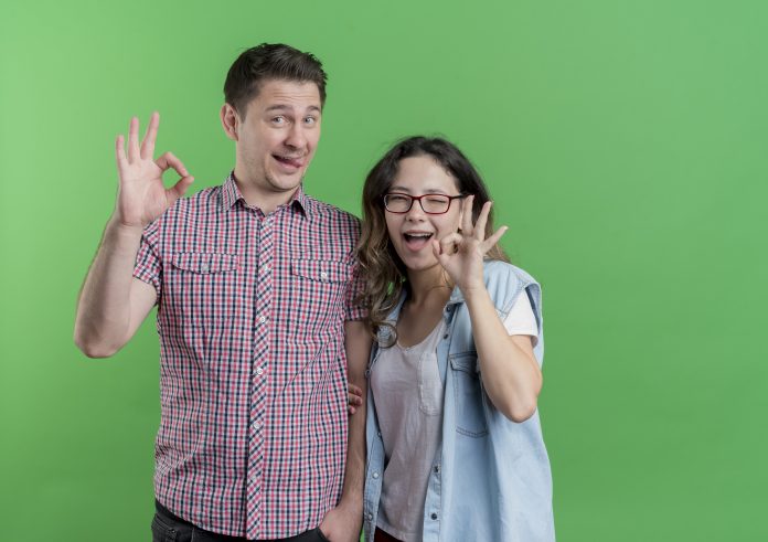 young couple man and woman in casual clothes happy and positive showing ok signs having fun together standing over green background